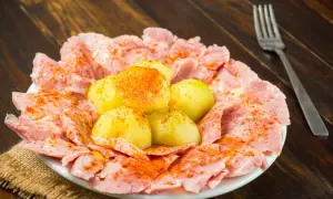 Plato de lacon con cachelos, patatas cocidas y pimentón, servido sobre una mesa de madera.
