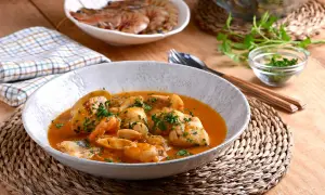 Deliciosa cazuela de pescado con gambas y trozos de pescado blanco en una salsa rojiza, adornada con perejil fresco.