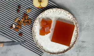 Un trozo de dulce de manzana y cubos cortados en un plato, junto a frutos secos y una manzana a medio cortar.