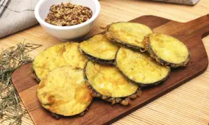 Berenjenas rebozadas con harina y huevo, doradas y crujientes, servidas en tabla de madera con un cuenco de mostaza.
