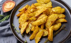 Patatas al horno crujientes y doradas, sazonadas con hierbas, servidas en un plato oscuro con una salsa cremosa y romero fresco.
