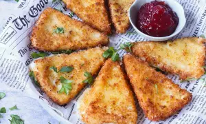 Triángulos de queso frito crujientes, servidos con un tazón de mermelada de frutos rojos.