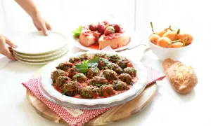 Albondigas de berenjenas en salsa roja, decoradas con albahaca, junto a un postre de fresas y pan.