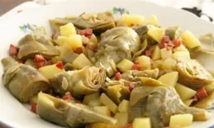 Plato de alcachofas tiernas y trocitos de patata, salpicado con dados de jamón serrano. Un bocado delicioso.