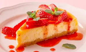 Deliciosa tarta de queso con fresas frescas y salsa de fresa, decorada con hojas de menta.