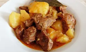 Plato de morcillo de ternera estofado con patatas y una hoja de laurel.