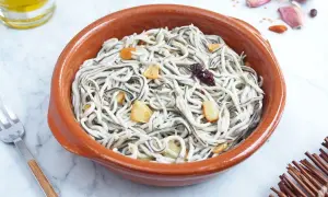 Un cuenco de barro con gulas al ajillo, salteadas con ajo y guindilla. Se ve un tenedor y una botella de aceite de oliva.