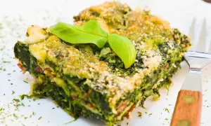 Porción de lasaña verde con capas de pencas de acelgas, queso y una hoja de albahaca encima.