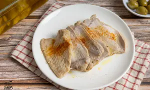 Lomo de orza tierno y jugoso, cortado en lonchas y espolvoreado con pimentón. Servido en plato blanco sobre mantel a cuadros.