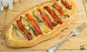 Coca de recapte con verduras asadas, pimientos rojos y cebolla sobre una base de pan rústico.