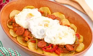 Huevos a la riojana servidos en una cazuela de barro, con patatas, chorizo y pimientos.
