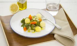 Plato de acelgas con patatas, zanahoria y cebolla, acompañado de limón, aceite de oliva y agua.