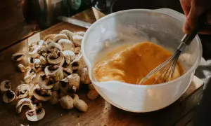 Un bol con huevos batidos y champiñones cortados en una tabla de madera, listos para un delicioso revuelto de setas.