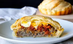 Porción de pastel de carne jugoso con huevo duro y salsa de tomate, envuelto en masa dorada.