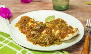 Un plato de urta a la roteña, con pescado blanco cubierto de cebolla y pimientos pochados, servido en una mesa de madera.