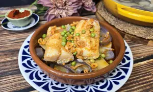 Bacalao a la gallega con patatas, guisantes y ajo frito en cazuela de barro. Un plato tradicional lleno de sabor.