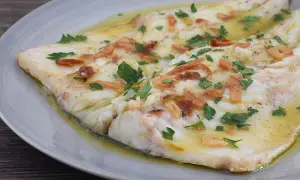 Lubina a la donostiarra, un plato de pescado blanco tierno bañado en aceite de oliva con láminas de ajo dorado y perejil fresco.