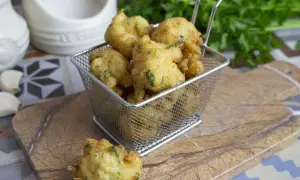 Buñuelos de bacalao dorados y crujientes, servidos en una cesta metálica. Perfectos para picar.