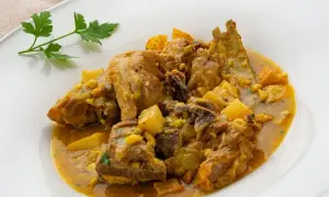 Choto al ajillo, un guiso tierno de cabrito con patatas y un toque de ajo, servido en un plato blanco.