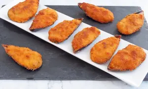 Mejillones tigre receta: mejillones rebozados y fritos, dorados y crujientes, servidos en una bandeja blanca sobre una pizarra.