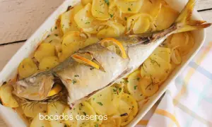 Un delicioso chicharro al horno con patatas, limón y romero, listo para servir.