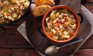 Un reconfortante guiso de pollo con patatas de la abuela, servido en cazuela de barro con pan tostado.
