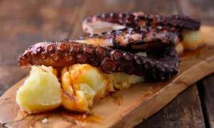 Pulpo tierno con patatas y pimentón, servido en tabla de madera.