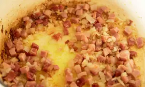 Guisantes con jamón, la receta de la abuela en plena cocción. Cebolla y taquitos de jamón dorándose en la sartén.