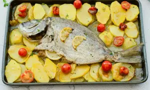 Delicioso sargo al horno con patatas y tomates cherry, listo para servir.