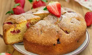 Delicioso bizcocho de fresa, espolvoreado con azúcar glas y decorado con una fresa fresca. Se ve una porción cortada, revelando trozos de fresa en su interior.