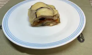 Un delicioso pastel de berenjenas gratinado con queso, servido en un plato blanco con borde azul.