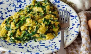 Un delicioso revuelto de espinacas cremoso, servido en un plato con salpicaduras azules. Un tenedor plateado descansa a un lado, listo para disfrutar.
