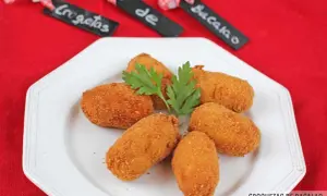 Croquetas de bacalao doradas y crujientes, servidas en un plato blanco con perejil.