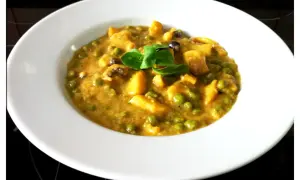 Plato de jibia en salsa de almendras, con guisantes y trozos de patata, decorado con una hoja verde.