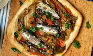 Deliciosa coca de verduras con sardinas y perejil fresco, servida sobre tabla de madera.