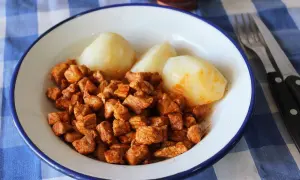 Plato de zorza con patatas cocidas, servido en un cuenco blanco con borde azul sobre un mantel de cuadros.