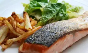 Un delicioso salmón a la plancha con piel crujiente, acompañado de patatas fritas doradas y una fresca ensalada verde.