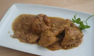 Sabroso pollo con almendras en una salsa dorada, servido en un plato blanco con una ramita de perejil.
