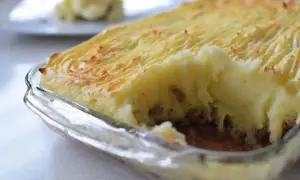 Un delicioso pastel de papa recién horneado, con una capa dorada y texturizada de puré de papa sobre un relleno jugoso.