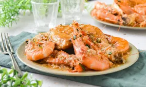 Plato de pollo con gambas en salsa cremosa, decorado con perejil picado. Un manjar listo para disfrutar.