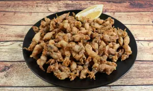 Un plato negro rebosante de puntillas de calamar crujientes, con un gajo de limón esperando para dar el toque final.