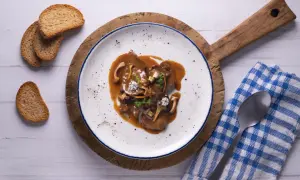 Fricandó de vedella amb bolets i una salsa espessa, servit en un plat blanc amb vores blaves, acompanyat de torradetes.