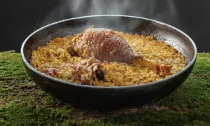 Arroz meloso con pitu de caleya, humeante y servido en paellera sobre un lecho de musgo.