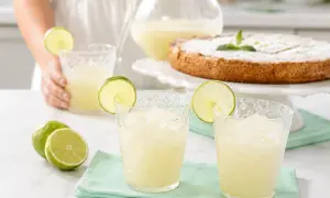 Refrescante granizado de limón servido en vasos con rodajas de lima, junto a limones frescos y un pastel.