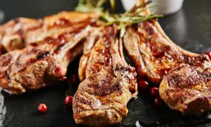 Chuletillas al sarmiento, jugosas y doradas, servidas con bayas rojas y romero sobre pizarra.