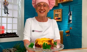 Eva Arguiñano sonríe con su delantal blanco y un gorro rosa, presentando una deliciosa tarta de queso.