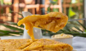 Un tenedor levanta un trozo jugoso de pincho de tortilla, mostrando su interior de patatas y huevo.
