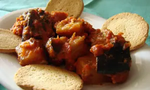 Berenjenas con tomate, un plato casero servido con tostas crujientes.