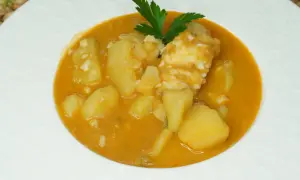 Un plato de patatas con bacalao en una salsa naranja, decorado con perejil.