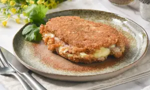 Libritos de lomo empanados, rellenos de queso y jamón, servidos en un plato rústico con cilantro y flores amarillas.